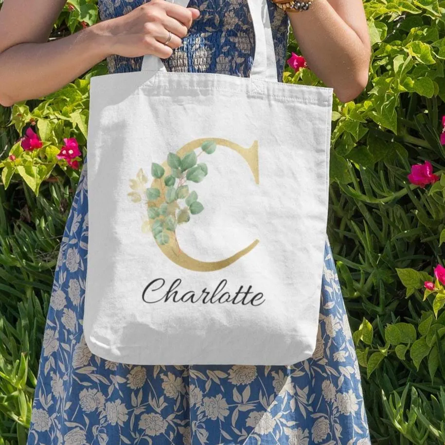 Personalised gold and sage green eucalyptus tote bag with letter C and name Charlotte, floral botanical design photographed outdoors