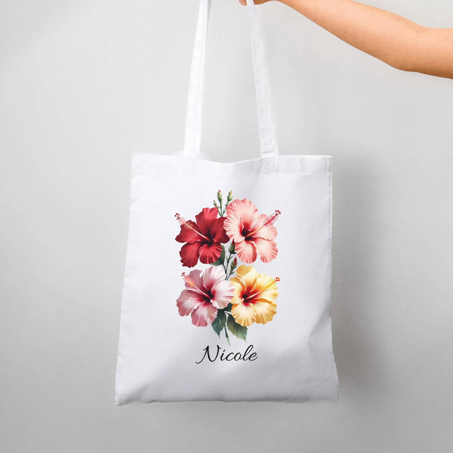 White tote bag with hibiscus floral design and 'Nicole' text on a light gray background