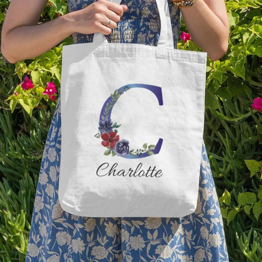 Custom floral initial C tote bag in indigo and burgundy design with name Charlotte held in garden setting