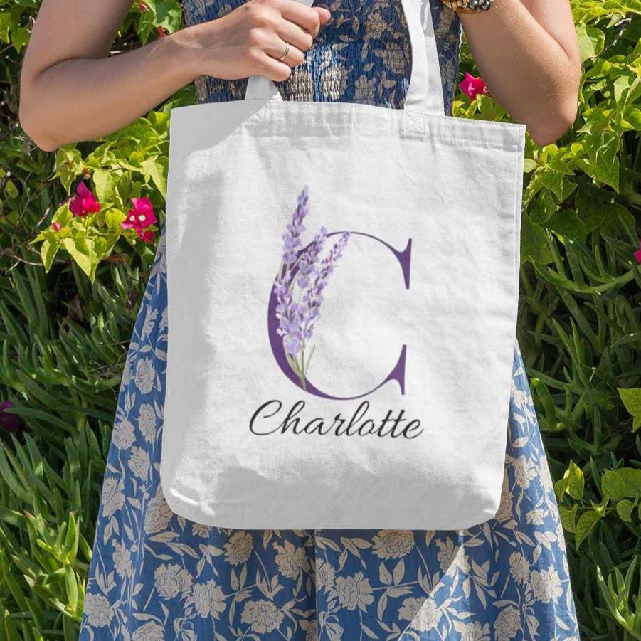 Close-up of Lavender Floral Custom Tote Bag With Purple Initial โCโ for Charlotte held outdoors among greenery