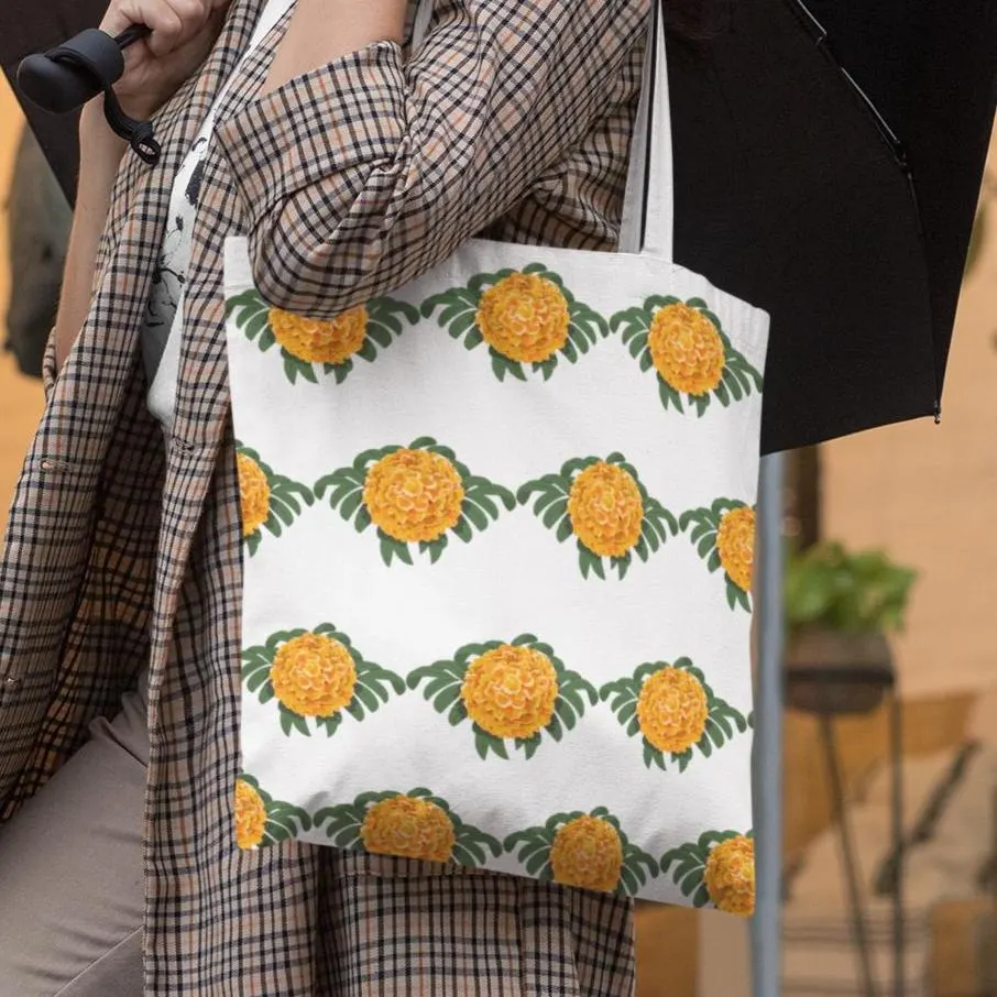 Woman carrying marigold patterned tote bag while walking in the city, showing bright floral design against plaid outfit