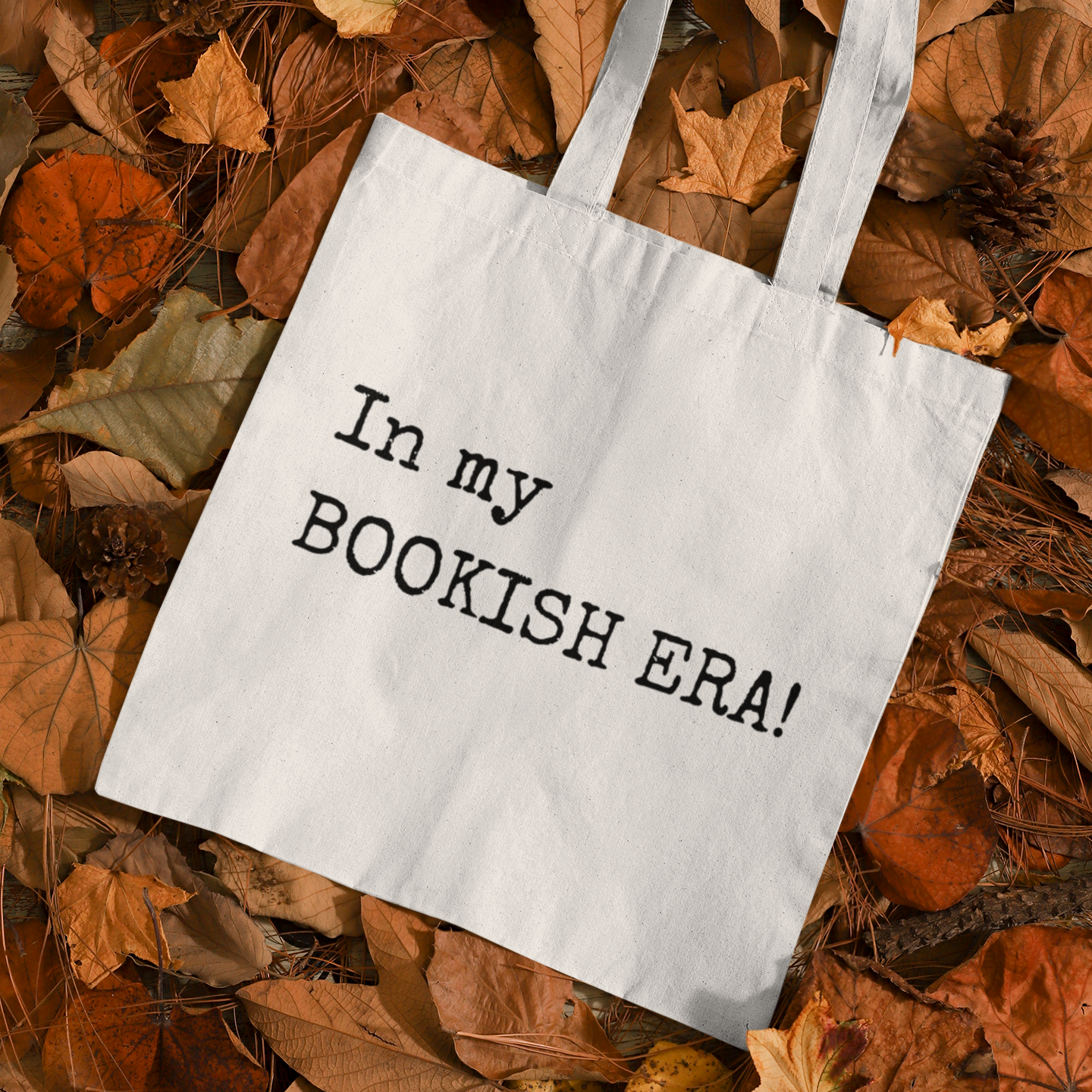“In my BOOKISH ERA!” tote bag placed on autumn leaves for a cozy seasonal aesthetic.