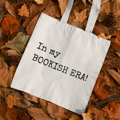 “In my BOOKISH ERA!” tote bag placed on autumn leaves for a cozy seasonal aesthetic.