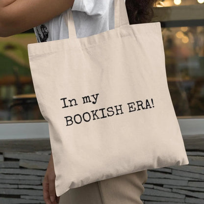 Person carrying beige “In my BOOKISH ERA!” tote bag, styled casually for everyday book lovers.