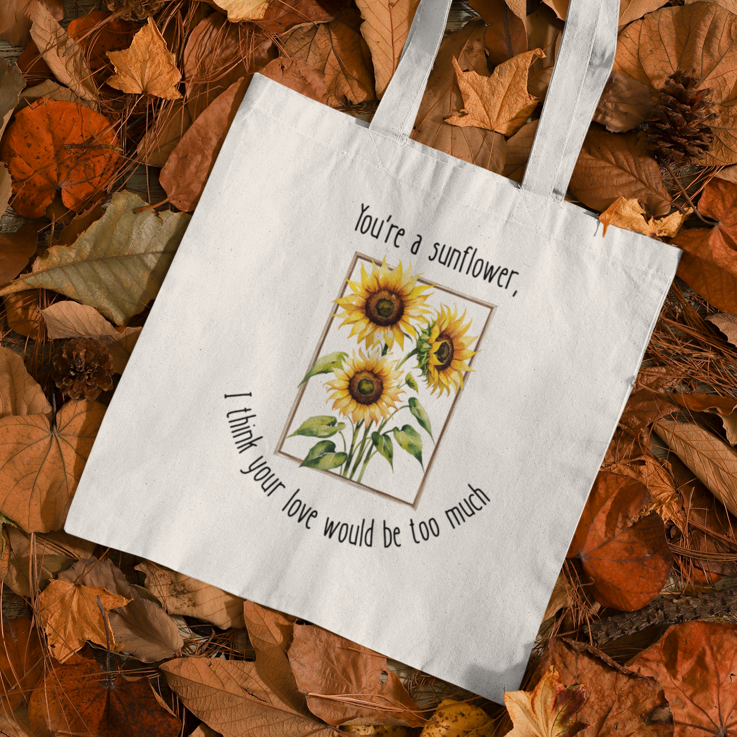 Tote bag with sunflower design and text on a bed of autumn leaves