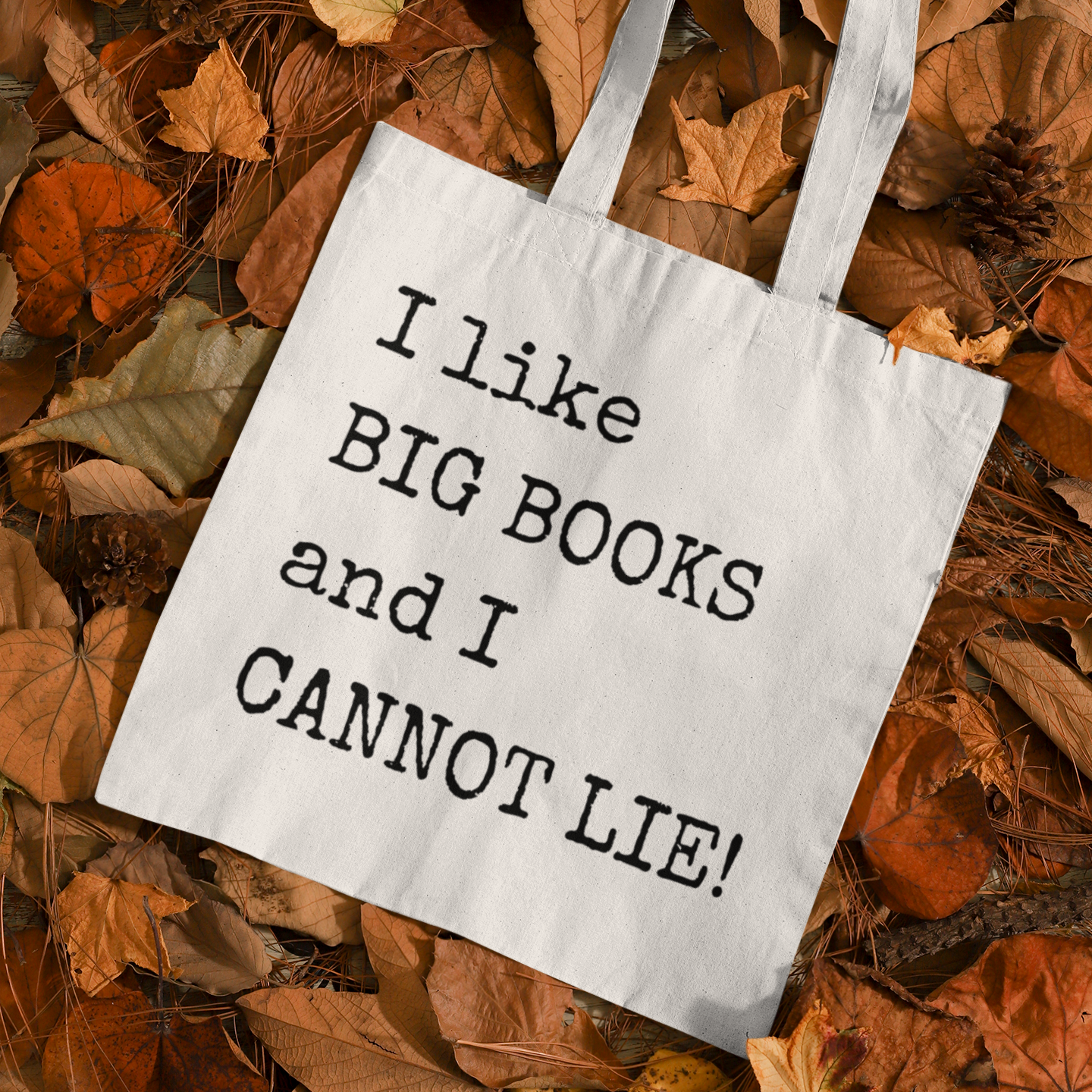 White canvas tote bag with “I like BIG BOOKS and I CANNOT LIE!” text, placed on autumn leaves – minimalist book lover tote