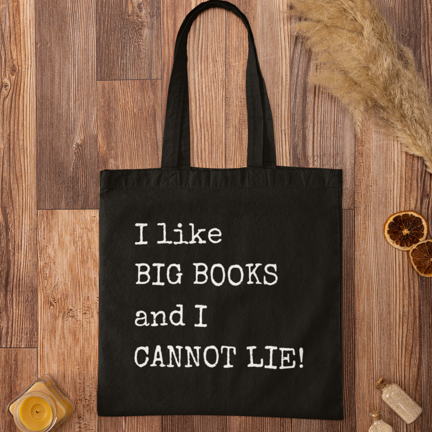 Black book lover tote bag with “I like BIG BOOKS and I CANNOT LIE!” printed in white, laid flat on rustic wood surface