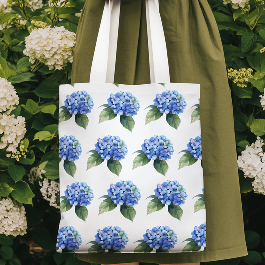 Woman holding Hydrangea Patterned Floral Design Tote Bag with blue hydrangea print surrounded by garden flowers