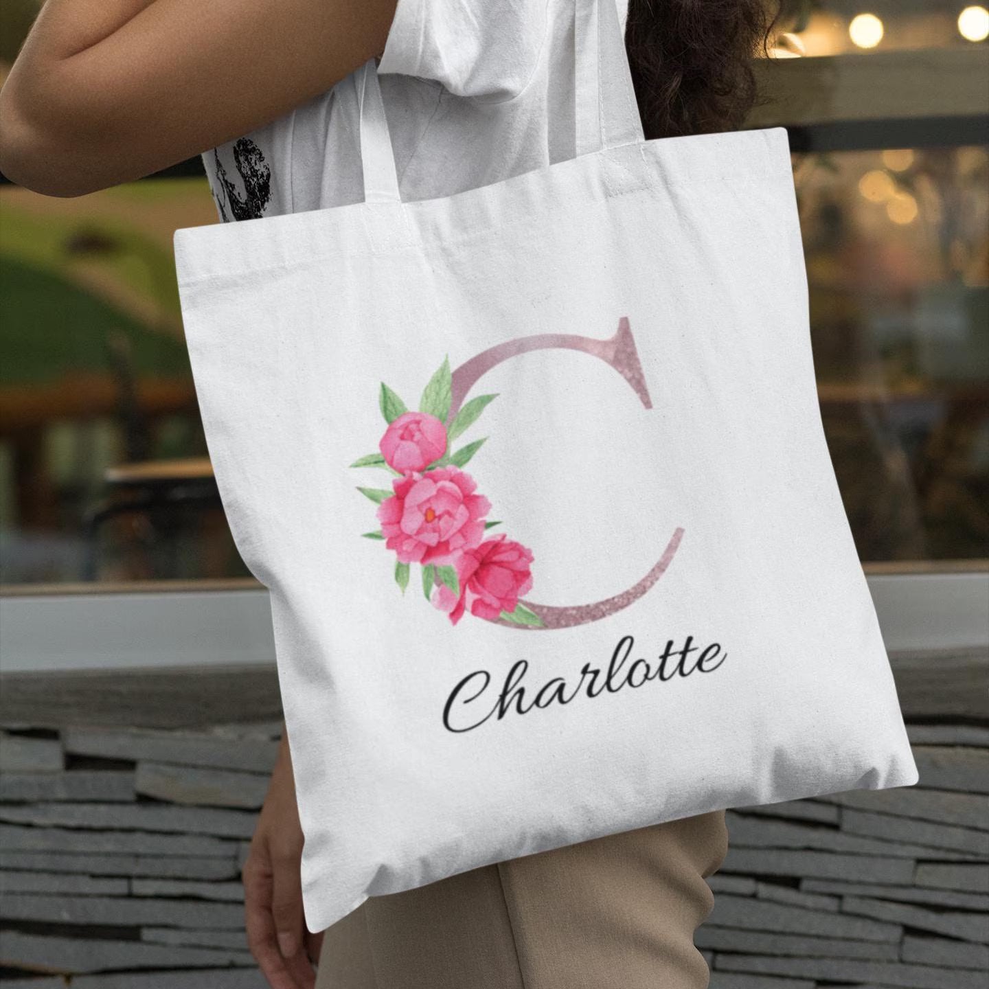 Close-up of blush pink floral initial C tote bag personalized with name Charlotte, held by woman in white blouse