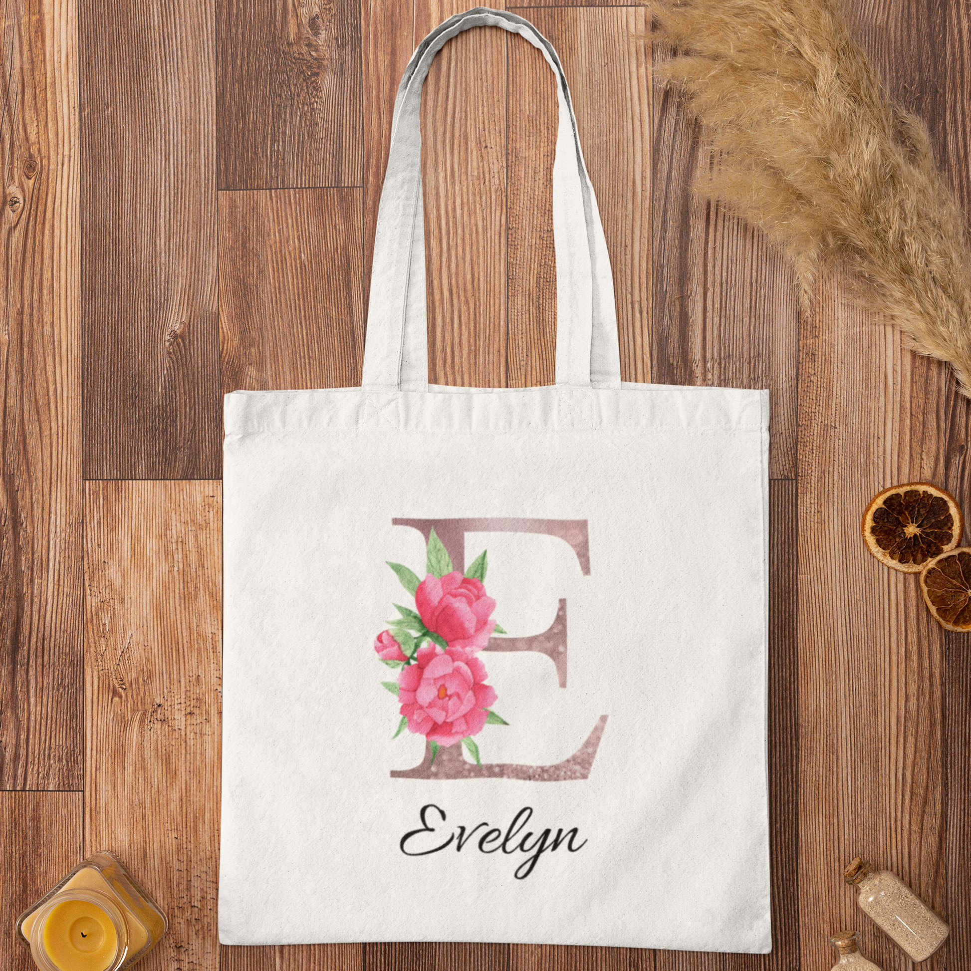 Flat lay of white tote bag with blush pink floral initial E and name Evelyn on wooden surface