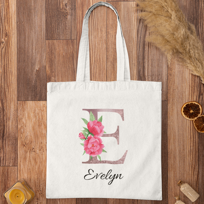 Flat lay of white tote bag with blush pink floral initial E and name Evelyn on wooden surface