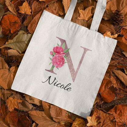 Personalized blush pink floral tote bag with initial N and name Nicole on autumn leaves background