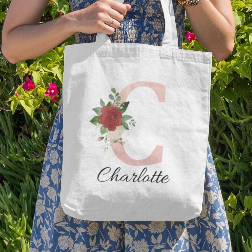 Woman holding Blush Pink and Roses Floral Custom Tote Bag with initial C and name Charlotte in a floral garden setting