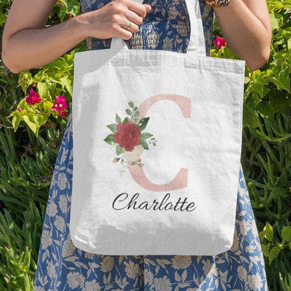 Woman holding Blush Pink and Roses Floral Custom Tote Bag with initial C and name Charlotte in a floral garden setting