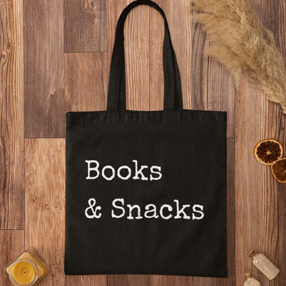 Books and Snacks black canvas tote bag flat lay on wooden background