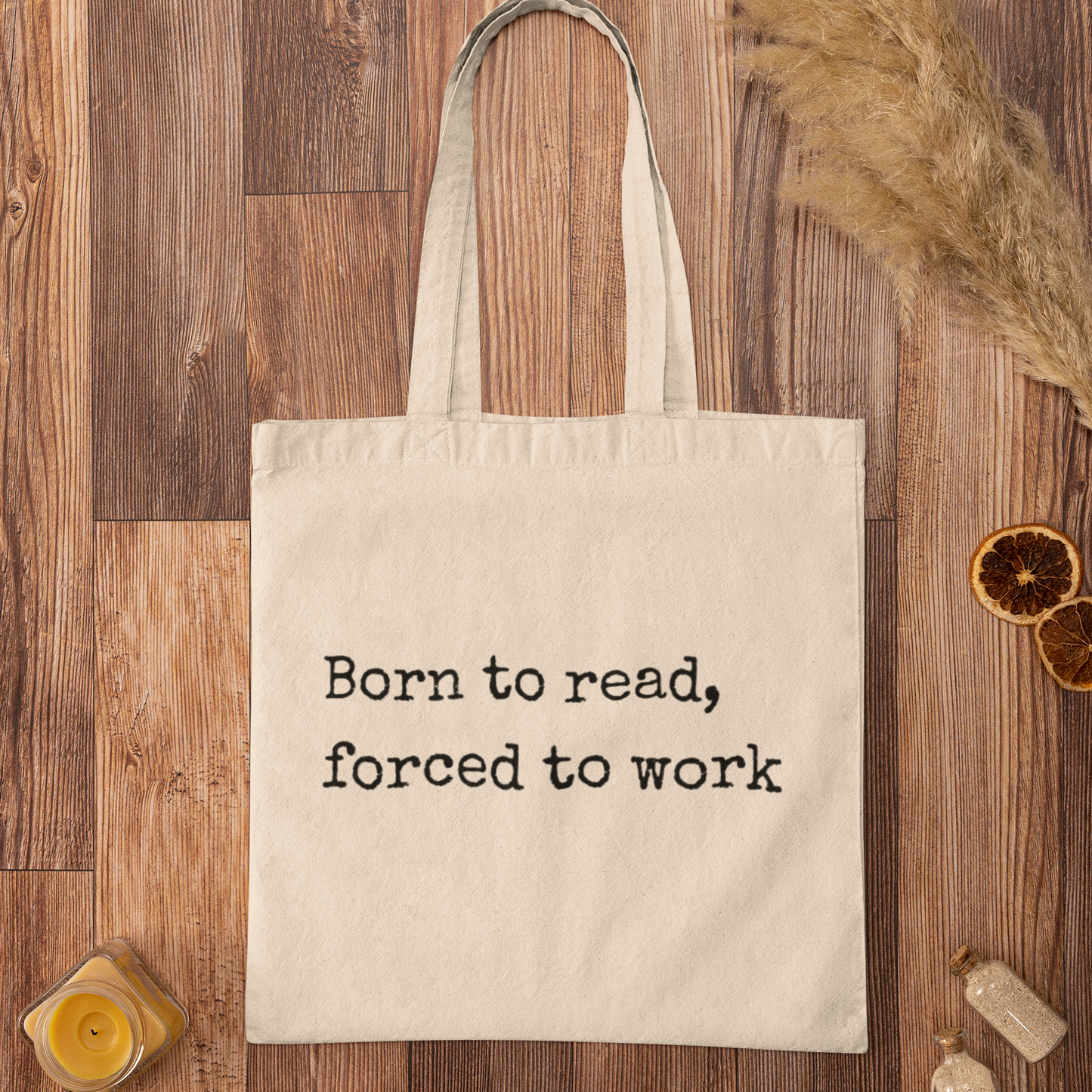 Beige “Born to read, forced to work” tote bag on wooden background — aesthetic flat lay