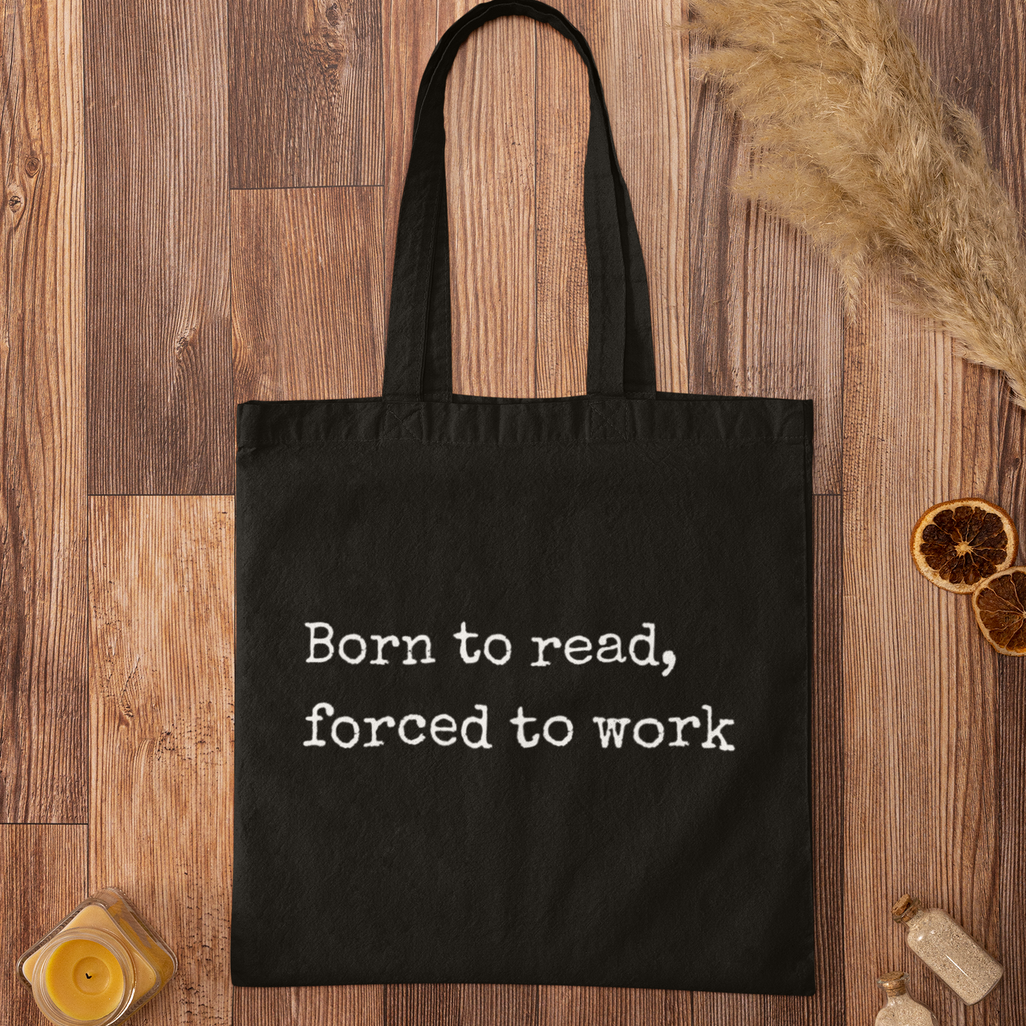 Black “Born to read, forced to work” tote bag flat lay on rustic wooden background