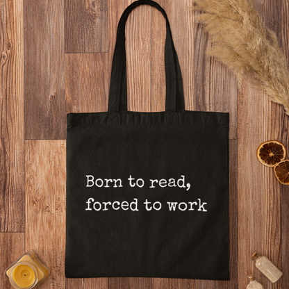 Black “Born to read, forced to work” tote bag flat lay on rustic wooden background
