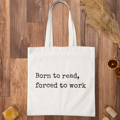 White “Born to read, forced to work” tote bag flat lay — minimalist design for readers