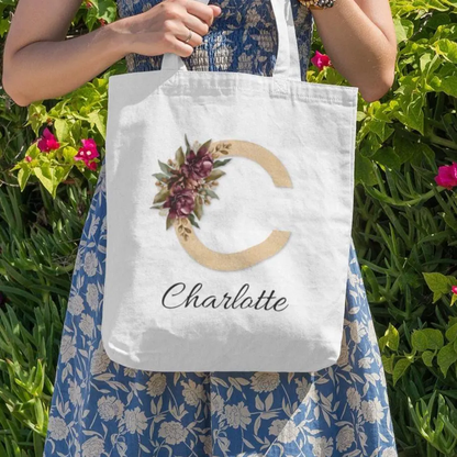 Woman holding personalized tote bag with gold initial C and burgundy flowers outdoors