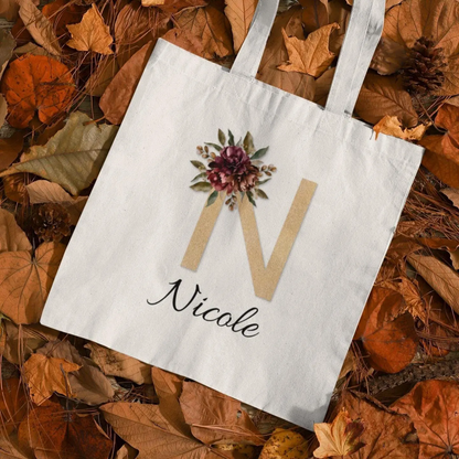 Custom tote bag with gold letter N and burgundy vintage floral design on autumn leaves background