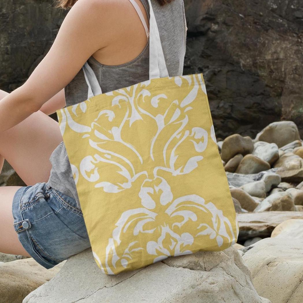 Butter yellow damask print tote bag photographed outdoors by rocks, ideal for travel or summer beach days