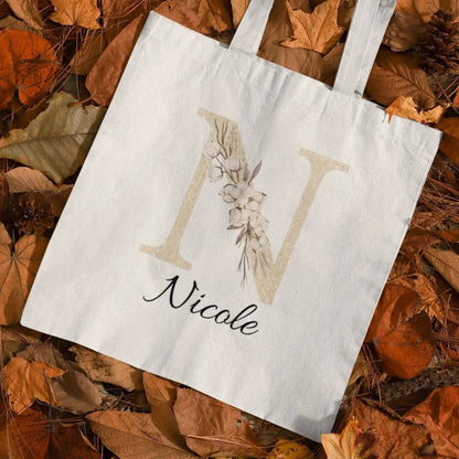 Champagne gold and ivory floral initial custom tote bag styled flat lay on autumn leaves background