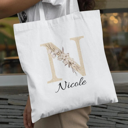 Outdoor lifestyle image of champagne gold and ivory floral initial custom tote bag worn over the shoulder