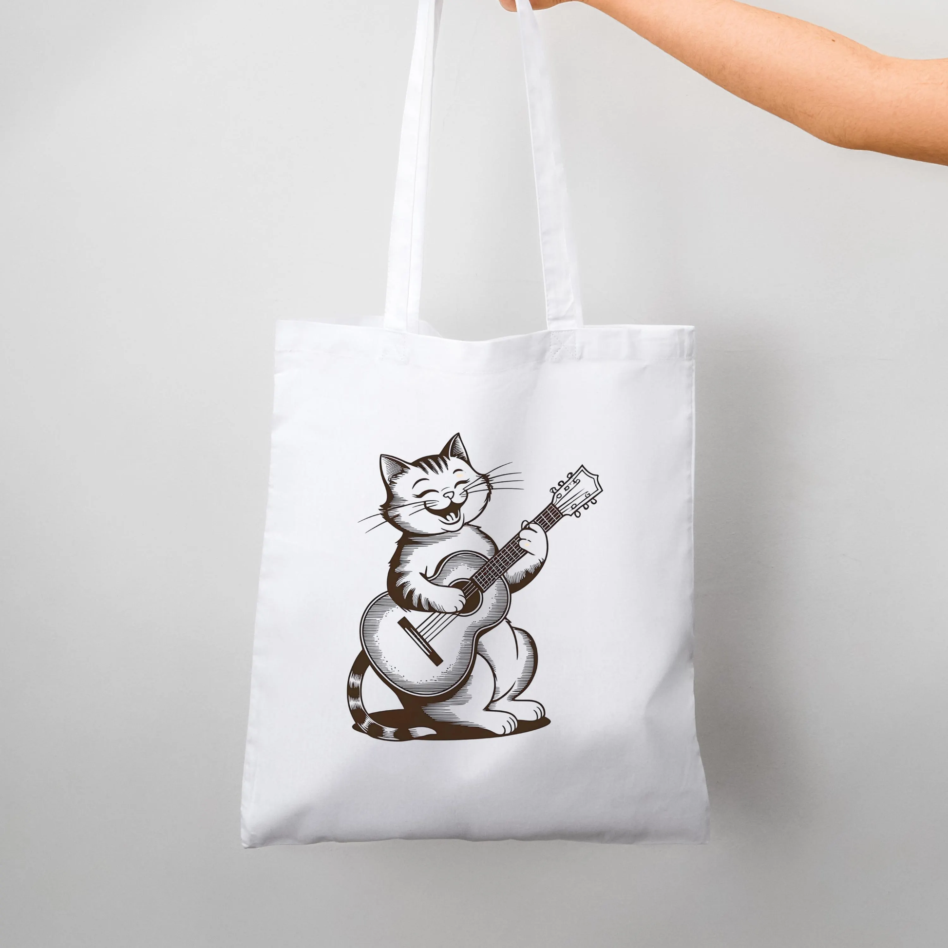 White minimalist tote bag with cute cat playing guitar design held in hand