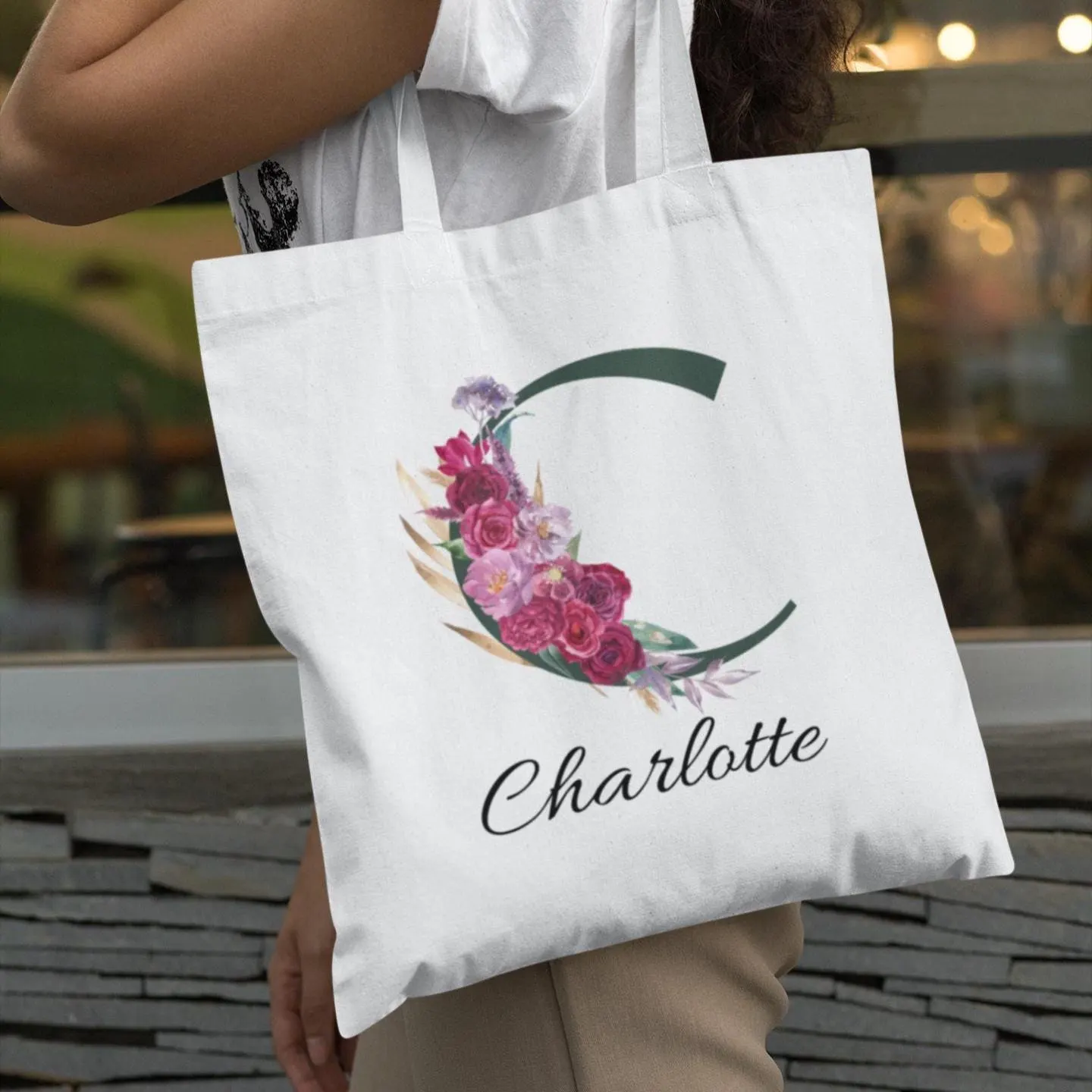 Elegant personalised tote bag with initial C and maroon floral accents carried by woman wearing white top and beige trousers