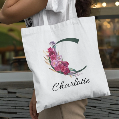 Elegant personalised tote bag with initial C and maroon floral accents carried by woman wearing white top and beige trousers