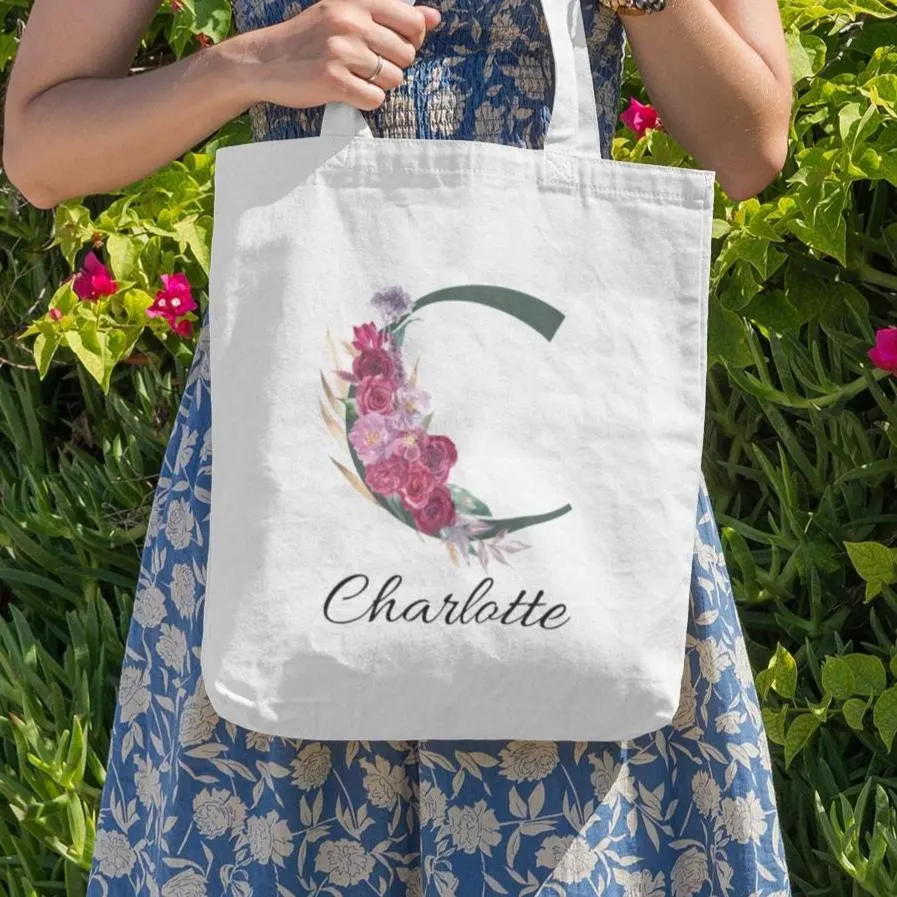Personalised forest green and maroon floral tote bag with initial C and name Charlotte displayed outdoors in floral setting
