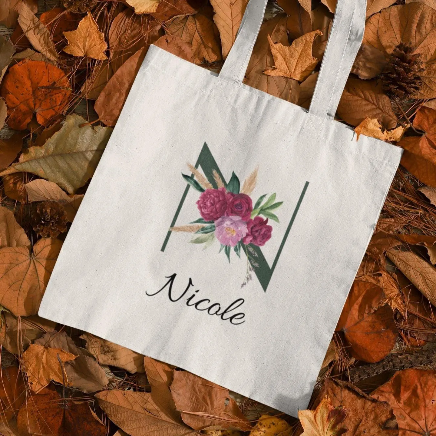 Custom tote bag featuring letter N with maroon and blush floral design and name Nicole placed on autumn leaves background