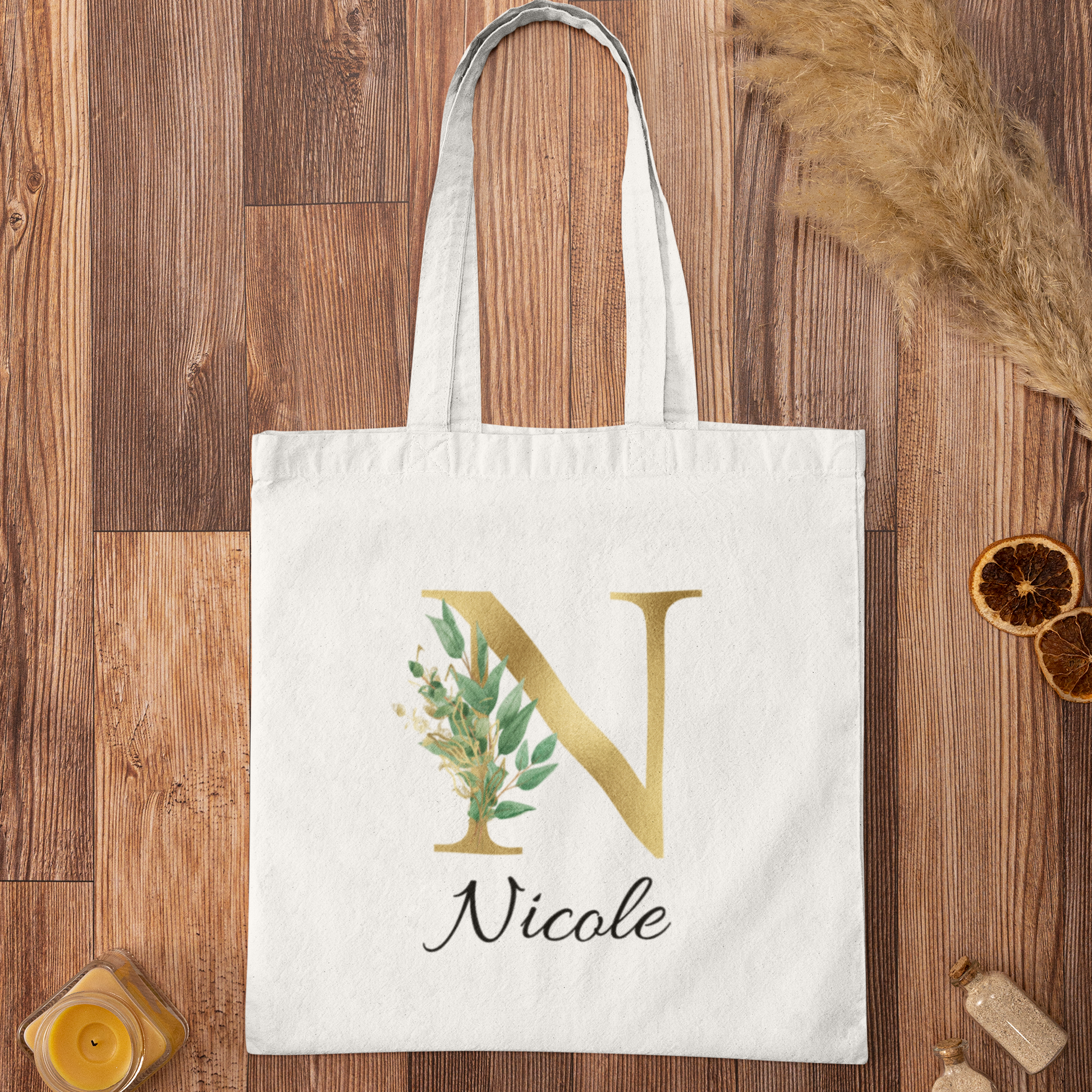 Personalised gold and sage green eucalyptus initial tote bag with letter N and name Nicole, placed on wooden background