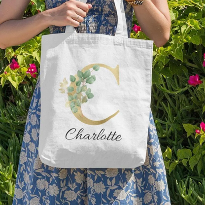 Personalised gold and sage green eucalyptus tote bag with letter C and name Charlotte, floral botanical design photographed outdoors
