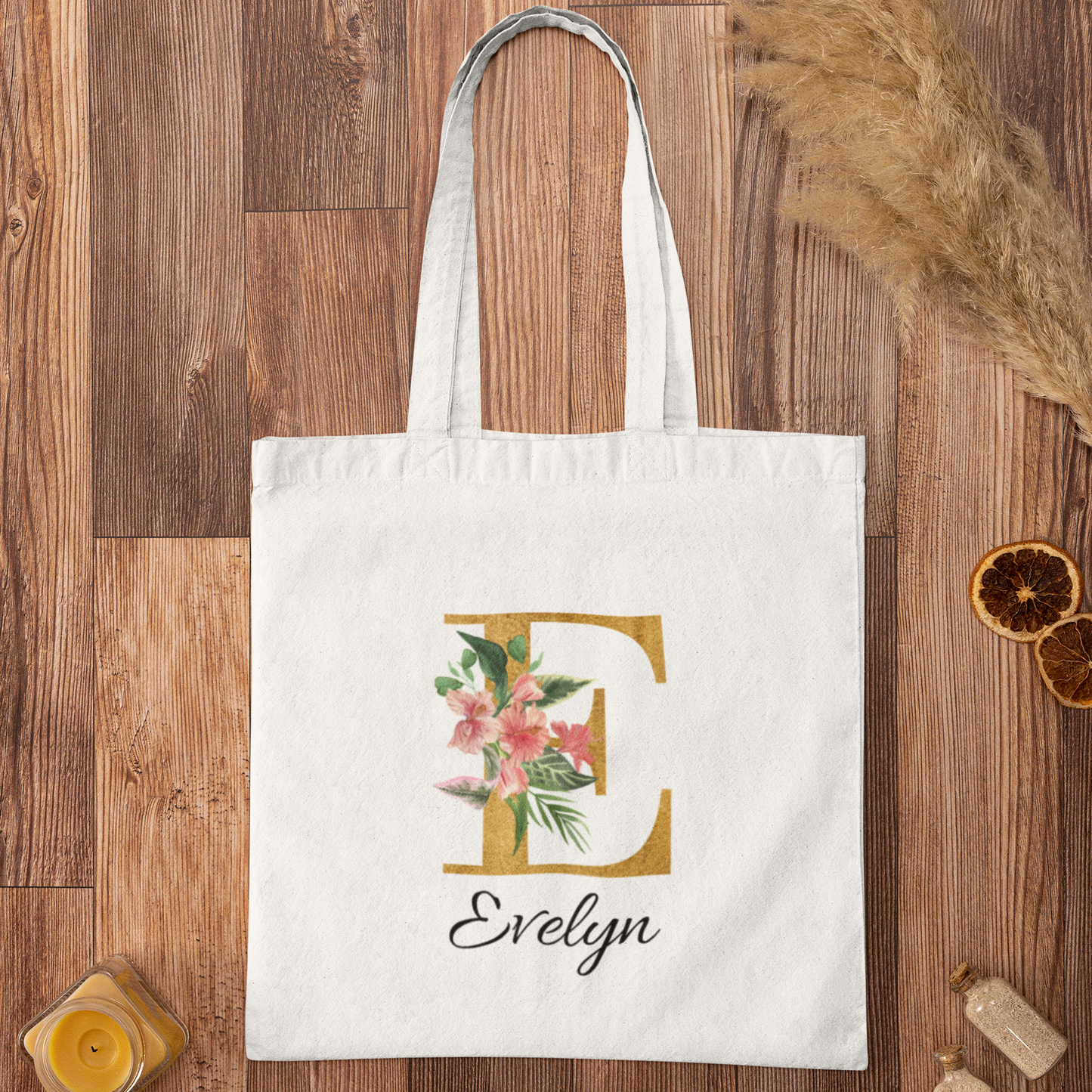 Hibiscus tropical floral custom tote bag with gold initial E and name Evelyn, laid flat on a wooden surface with warm rustic decor