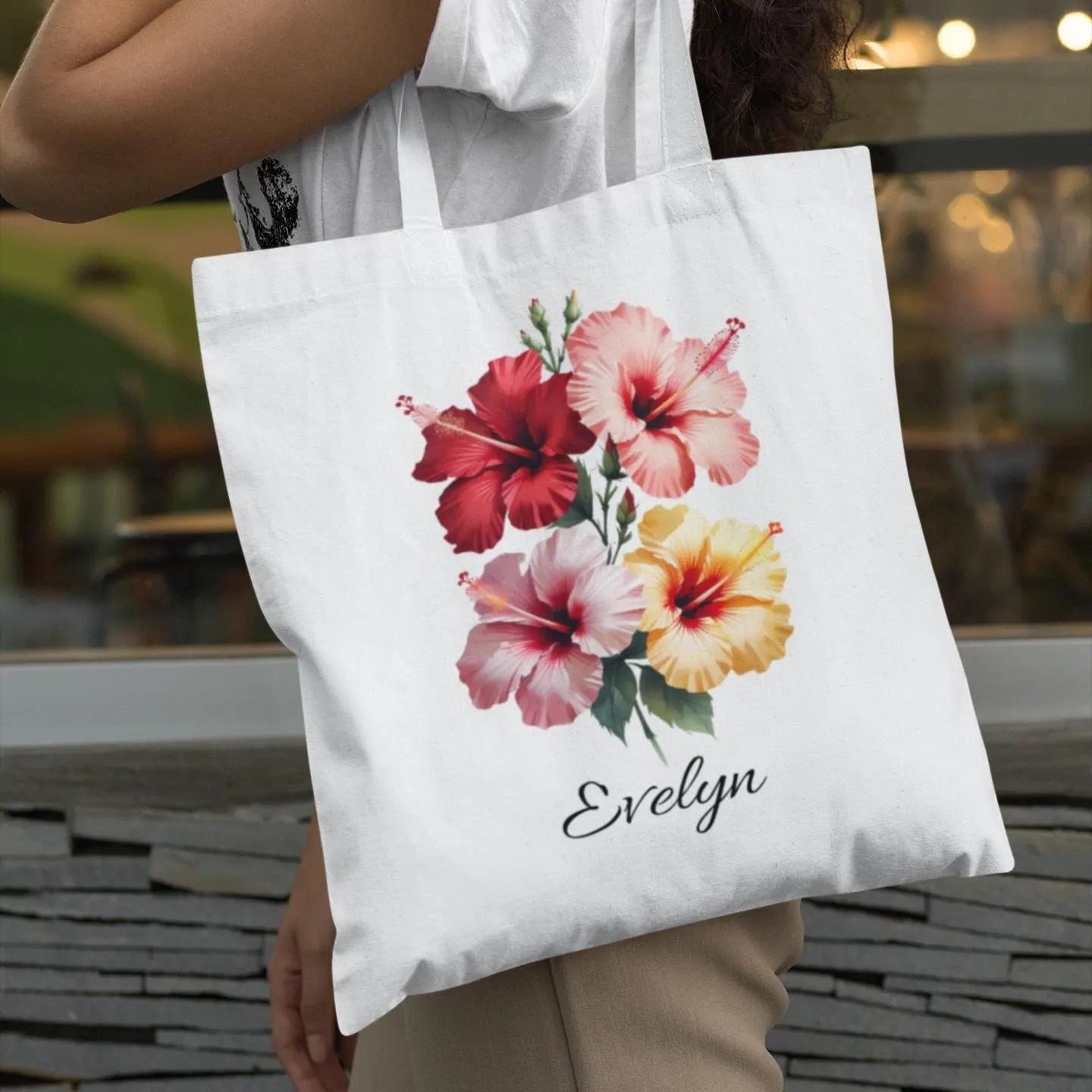 Tote bag with hibiscus floral design and 'Evelyn' text held by a person outdoors.