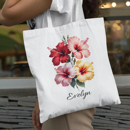 Tote bag with hibiscus floral design and 'Evelyn' text held by a person outdoors.