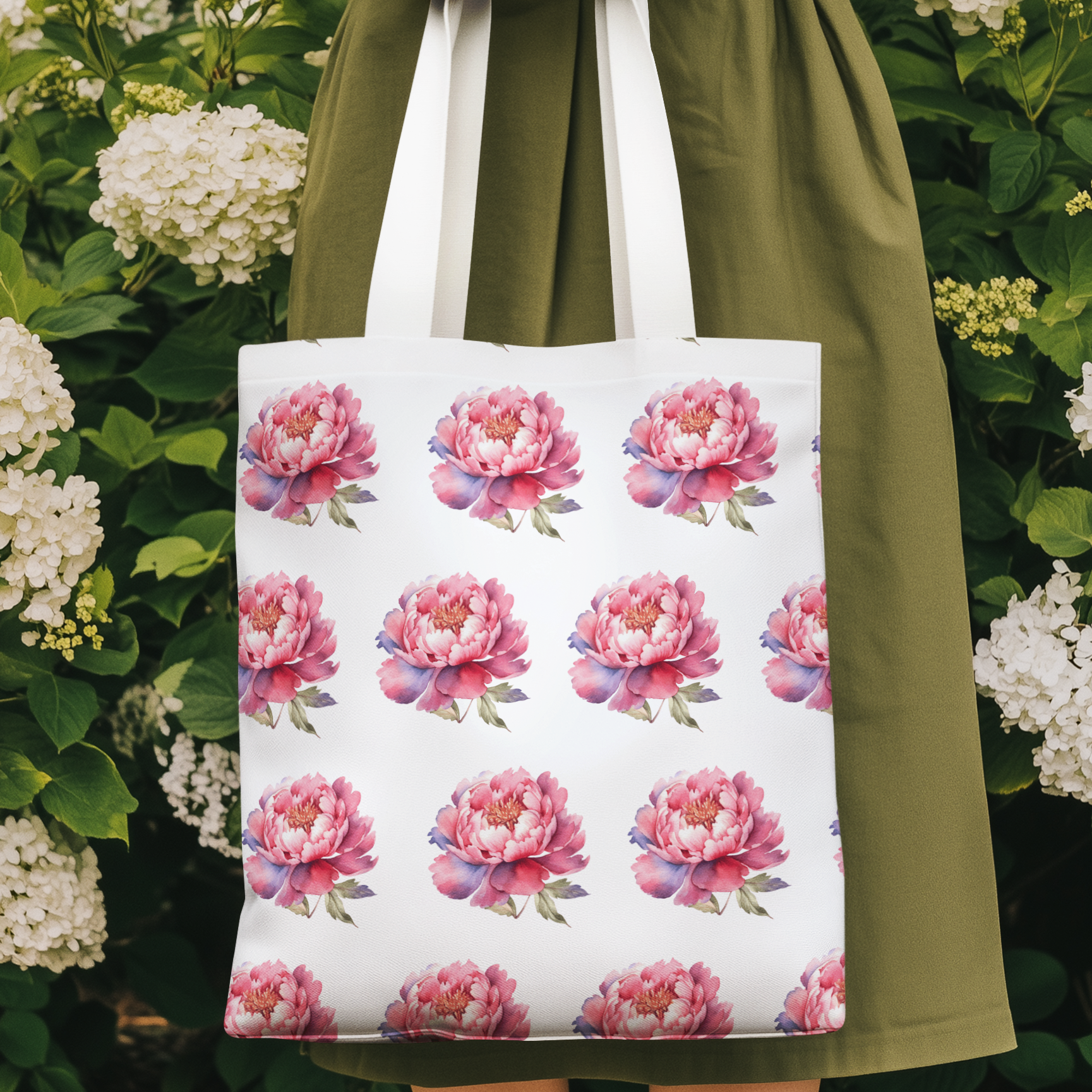 Pink peony floral pattern tote bag with watercolor peony print held outdoors among blooming hydrangeas