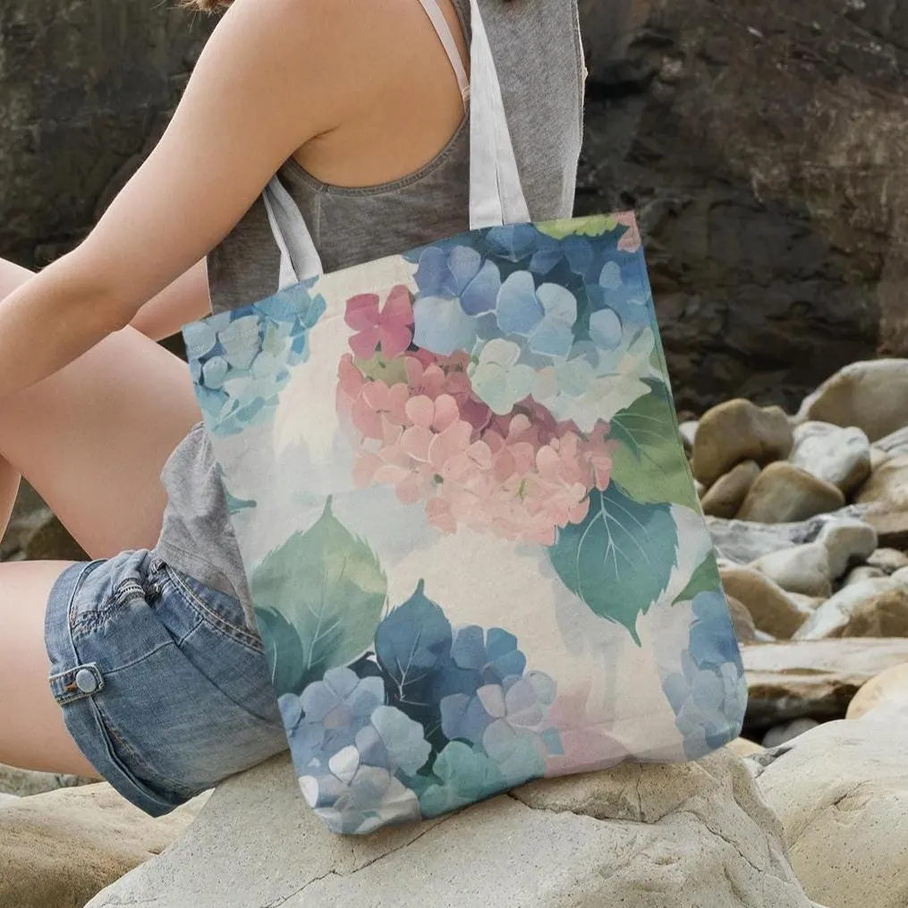 Floral tote bag with hydrangea print resting on rocks, pastel pink and blue flowers in abstract watercolor style
