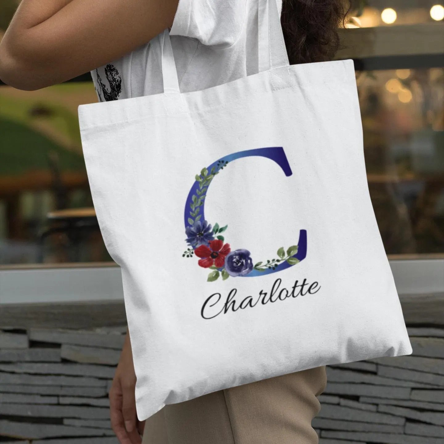 Personalized indigo and burgundy floral initial C tote bag carried outdoors by woman wearing white top