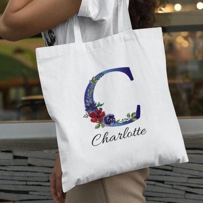 Personalized indigo and burgundy floral initial C tote bag carried outdoors by woman wearing white top
