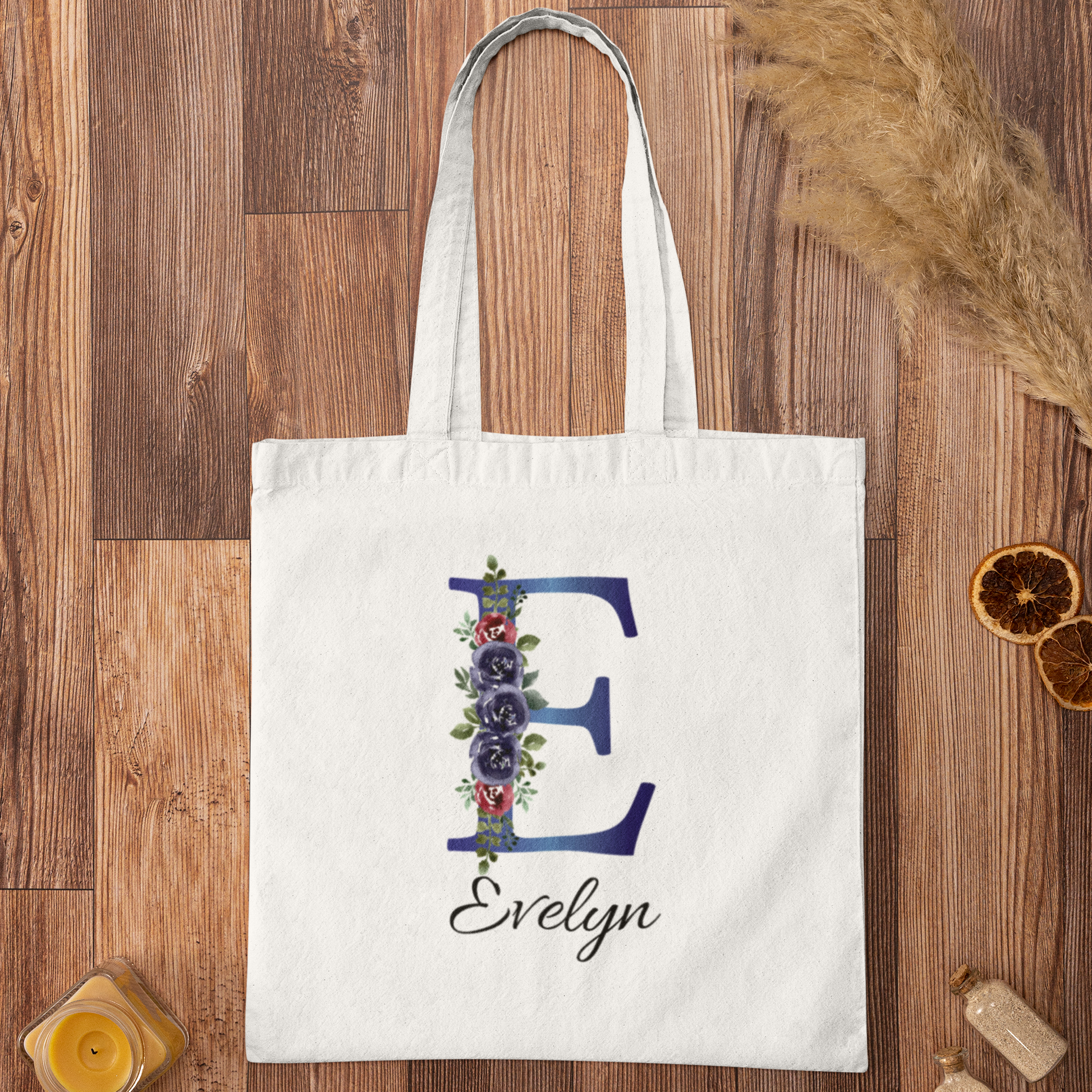 Flat lay of indigo and burgundy floral initial E tote bag with name Evelyn on rustic wooden background