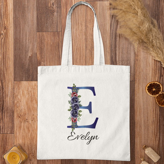 Flat lay of indigo and burgundy floral initial E tote bag with name Evelyn on rustic wooden background