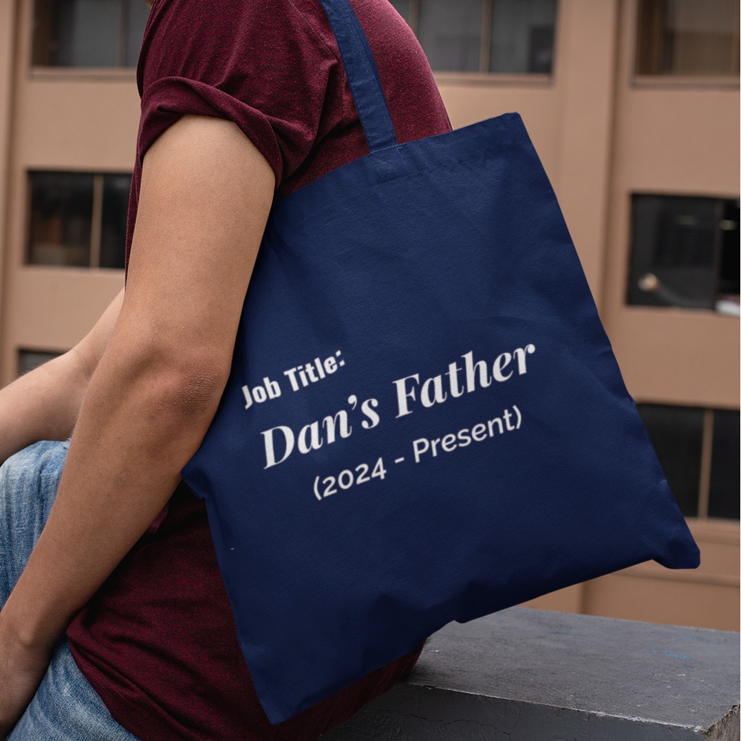 Man carrying personalized new dad tote bag with Dan’s Father Job Title design in navy