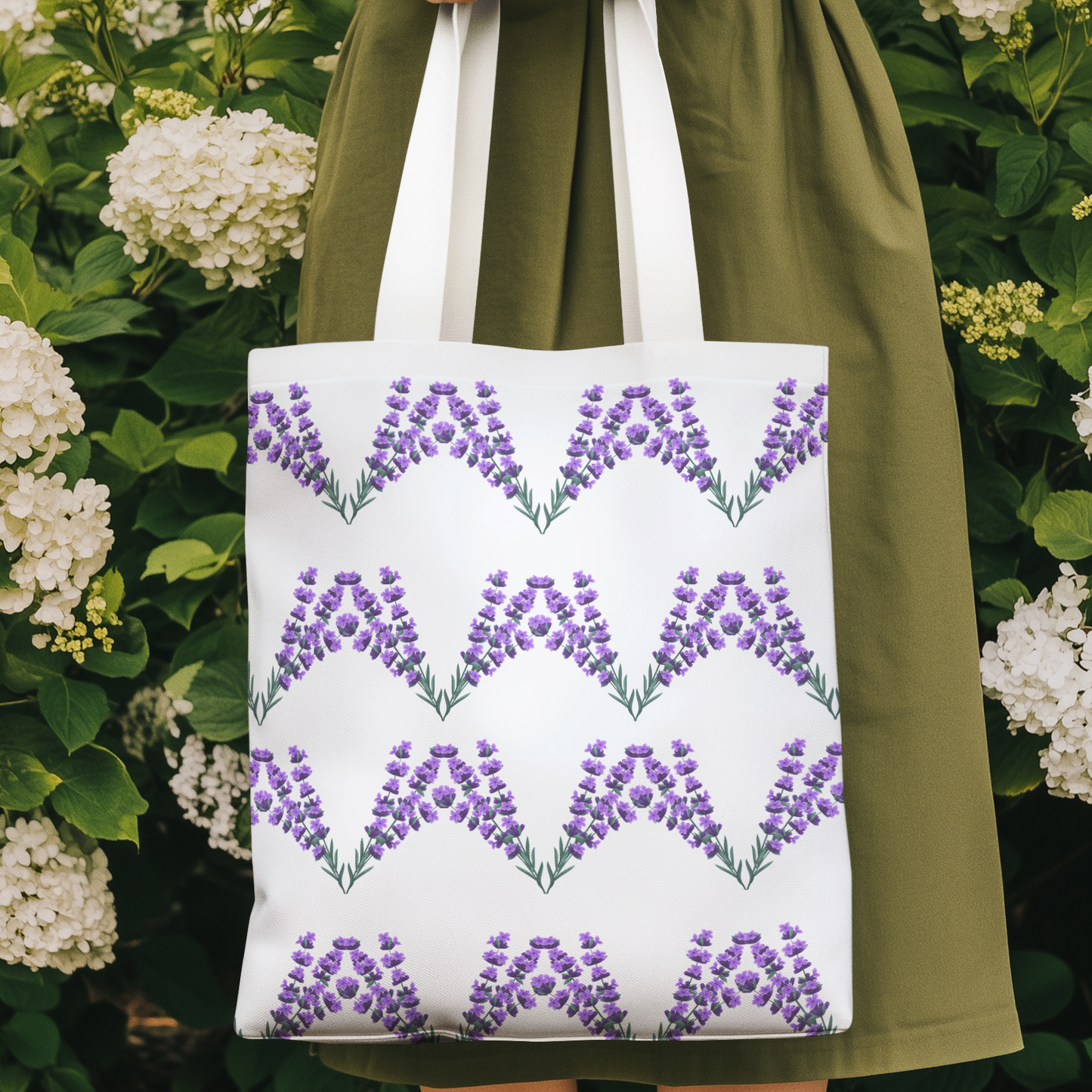 Lavender flower design patterned tote bag held in a garden surrounded by white hydrangeas, eco-friendly reusable floral tote