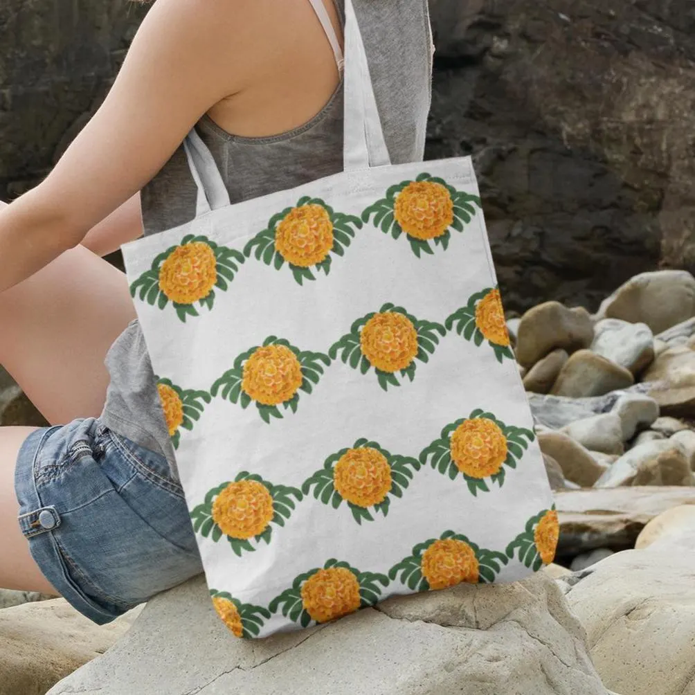 Marigold floral tote bag resting on rocks by the beach, featuring vivid orange flower pattern with green leaves