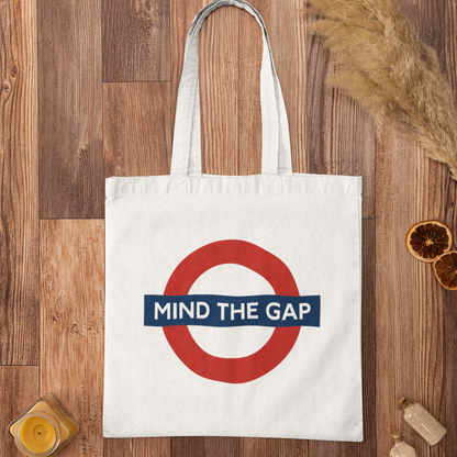 Mind The Gap graphic tote bag flatlay on rustic wooden background – eco-friendly London city streetwear bag