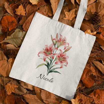 Tote bag with tiger lily floral design and 'Nicole' text on a bed of autumn leaves