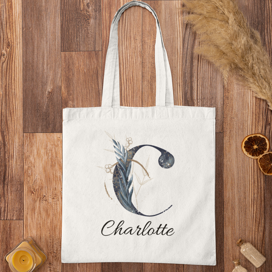 Midnight botanical tote bag with letter C and name Charlotte on wooden surface, custom navy and gold design